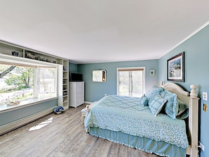 A bedroom with a large window, a bed with floral bedding, a dresser, and a television on top.