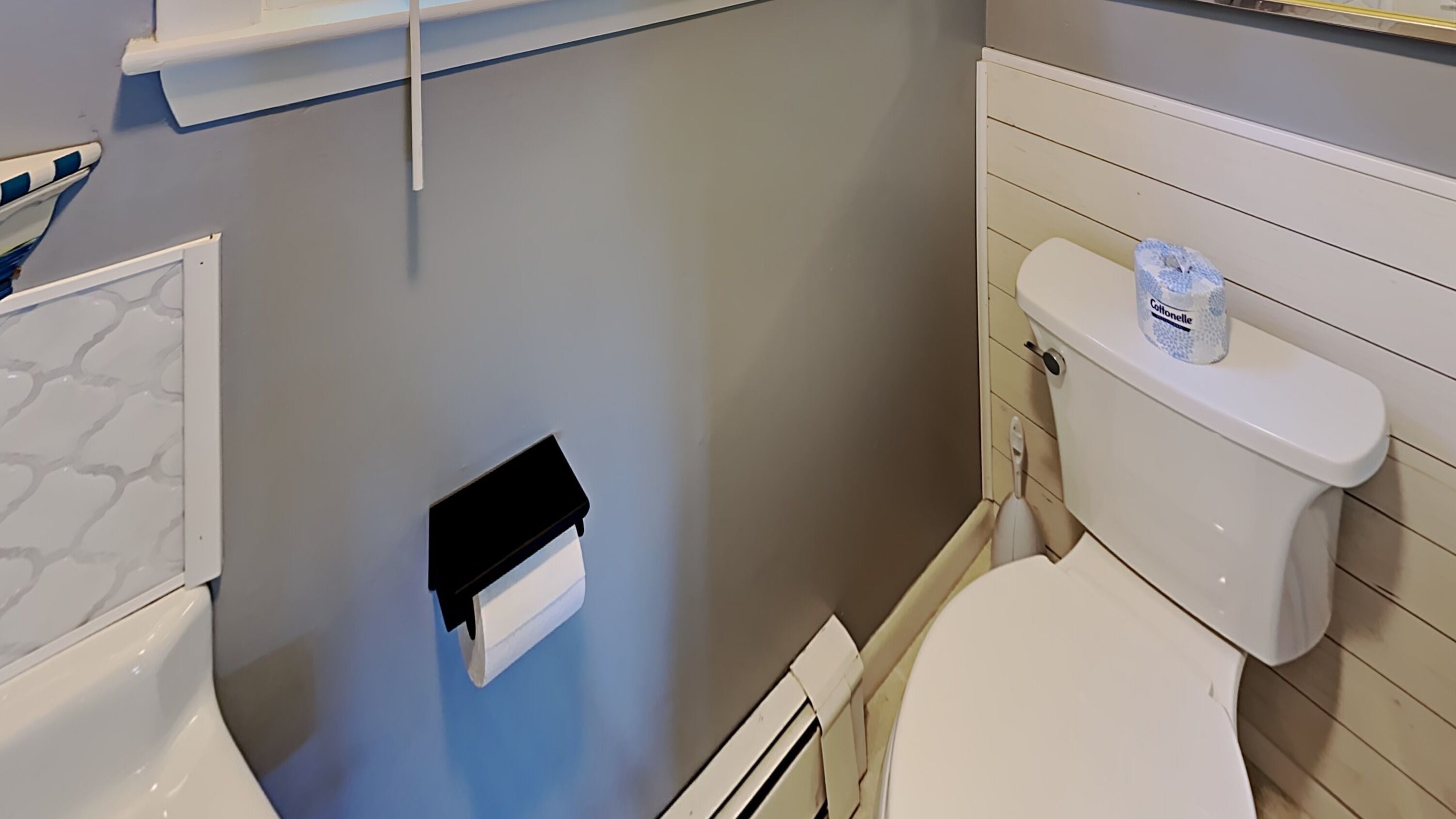 Un bagno con un WC, uno scaffale bianco sopra il water e un porta carta igienica bianco.