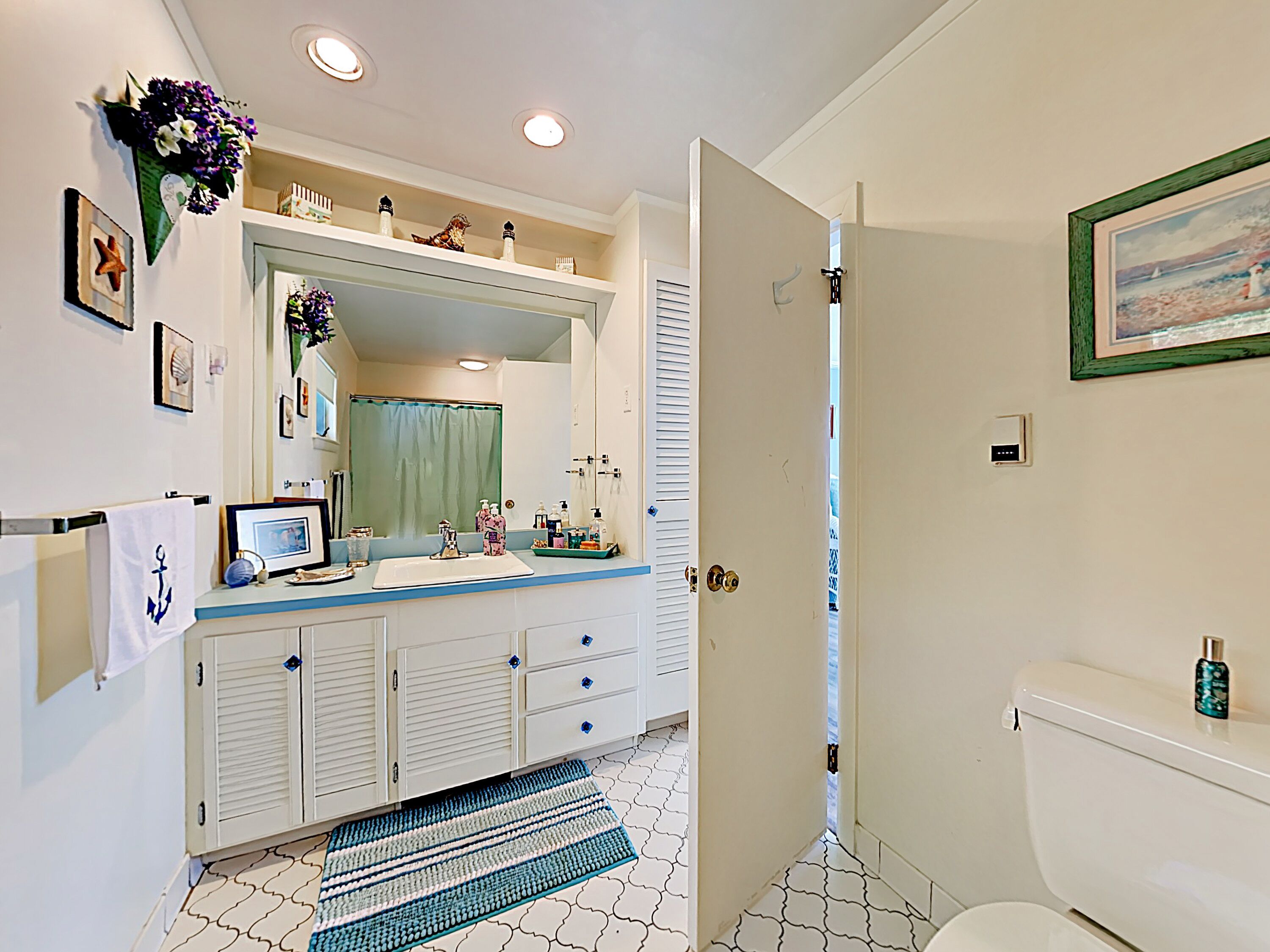 A bathroom with a white toilet, a sink with a mirror above it, a shower curtain, and a small shelf with toiletries.