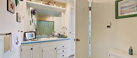 A bathroom with a white toilet, a sink with a mirror above it, a shower curtain, and a small shelf with toiletries.