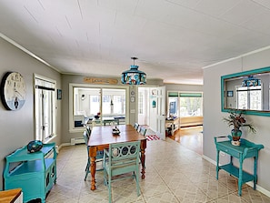 A spacious kitchen with a wooden table, teal furniture, and a hanging chandelier.