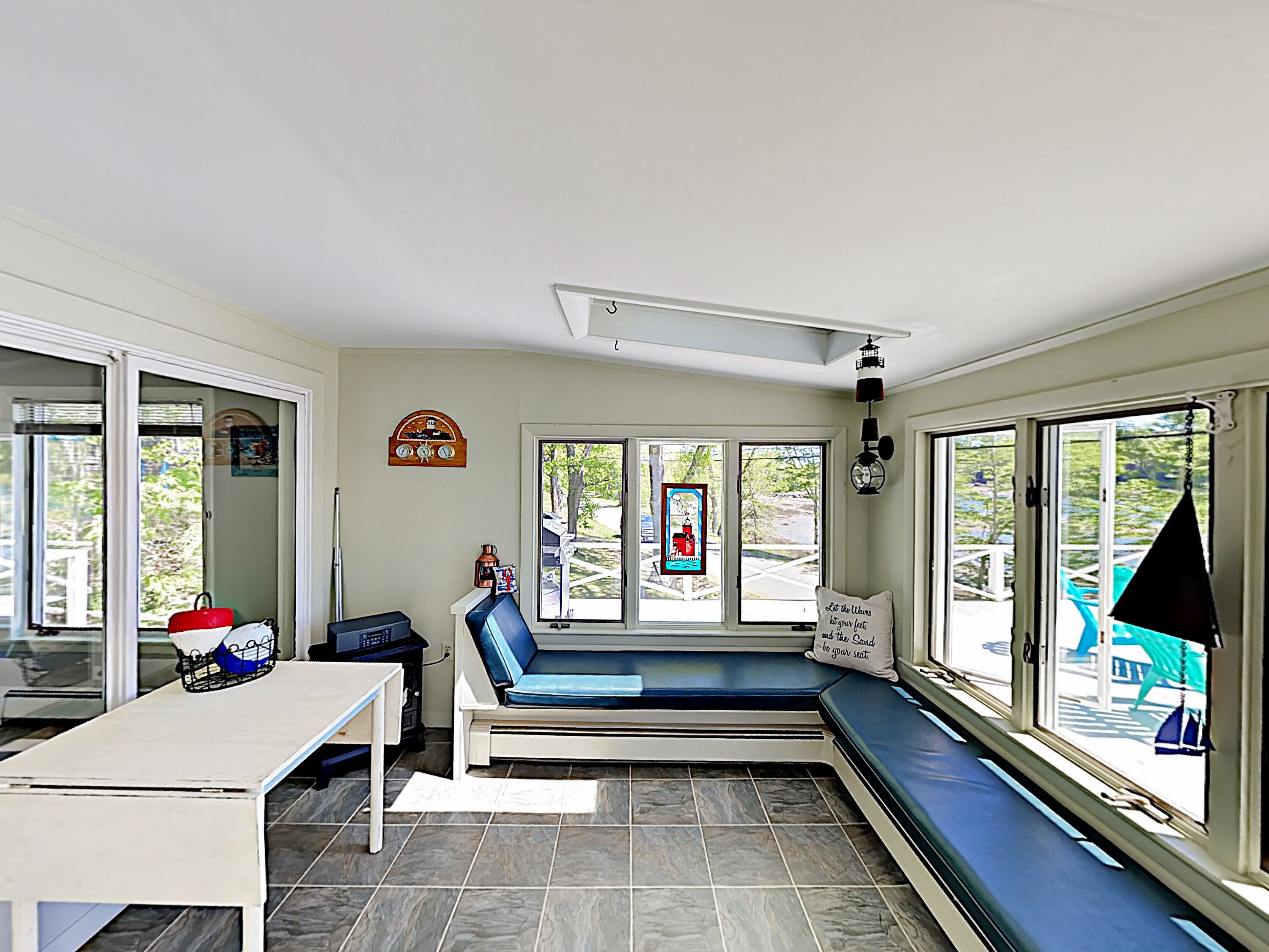 A room with a large window, a bench, a table, and a wall clock.