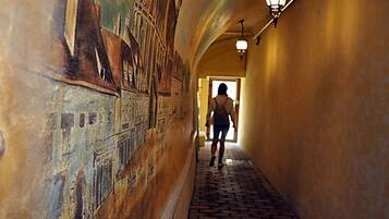 Una persona cammina lungo un corridoio con un murale sulla parete e un pavimento in mattoni.