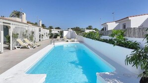 A rectangular swimming pool with a white deck, surrounded by a white fence and palm trees. - Velsuites (San Bartolome de Tirajana)