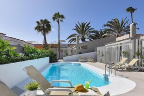 A swimming pool with lounge chairs, palm trees, and a white fence. - Velsuites (San Bartolome de Tirajana)