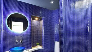 A bathroom with blue mosaic tiles, a round mirror, a white sink, and a toilet. - Velsuites (San Bartolome de Tirajana)