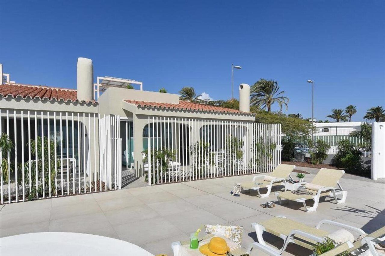 Un patio en la azotea con sillones blancos, una mesa y una valla.