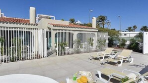 A rooftop patio with white lounge chairs, a table, and a fence. - Velsuites (San Bartolome de Tirajana)