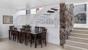 A dining area with a glass table surrounded by wooden chairs, a decorative white partition, and a stone accent wall. - Family Time and a Fire Pit 3 Bdr 2.5 Bth (Anchorage)