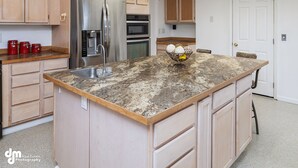 A kitchen with wooden cabinets, a stainless steel refrigerator, an oven, and a granite countertop. - Family Time and a Fire Pit 3 Bdr 2.5 Bth (Anchorage)