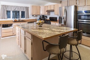 A kitchen with wooden cabinets, a granite countertop, stainless steel appliances, and a bar stool.
