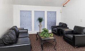 A modern lounge area with black leather sofas, a central table with plants, and patterned wallpaper.