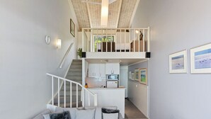 Ein modernes Interieur mit einer Treppe zu einem Schlafzimmer im Zwischengeschoss, einer Küchenzeile und einem Wohnzimmer mit einer Couch.