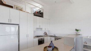 A modern kitchen with white cabinetry, a built-in oven, and a central island with a vase and bowl. - 5 Whitecrest Resort - Pool & Amazing Ocean Views (Wongarra)