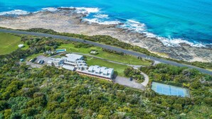 An aerial view of a coastal property with a large building, a tennis court, and a road leading to the beach. - 5 Whitecrest Resort - Pool & Amazing Ocean Views (Wongarra)