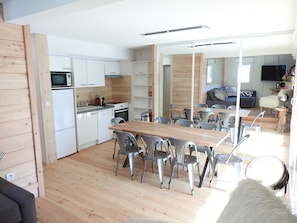 A modern kitchen with white cabinets, a microwave, and a dishwasher. There is a dining area with a wooden table and metal chairs.