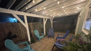 Ein überdachter Patio-Bereich mit mehreren blauen Stühlen, einem Topfpflanzen und Lichterketten.