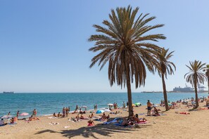 Une plage bordée de palmiers, des gens qui prennent un bain de soleil et un navire à l’horizon.