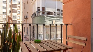 A balcony with a wooden table and bench, a green ashtray, and a view of a building with multiple windows and balconies. - Malagueta - Maestranza (Málaga)