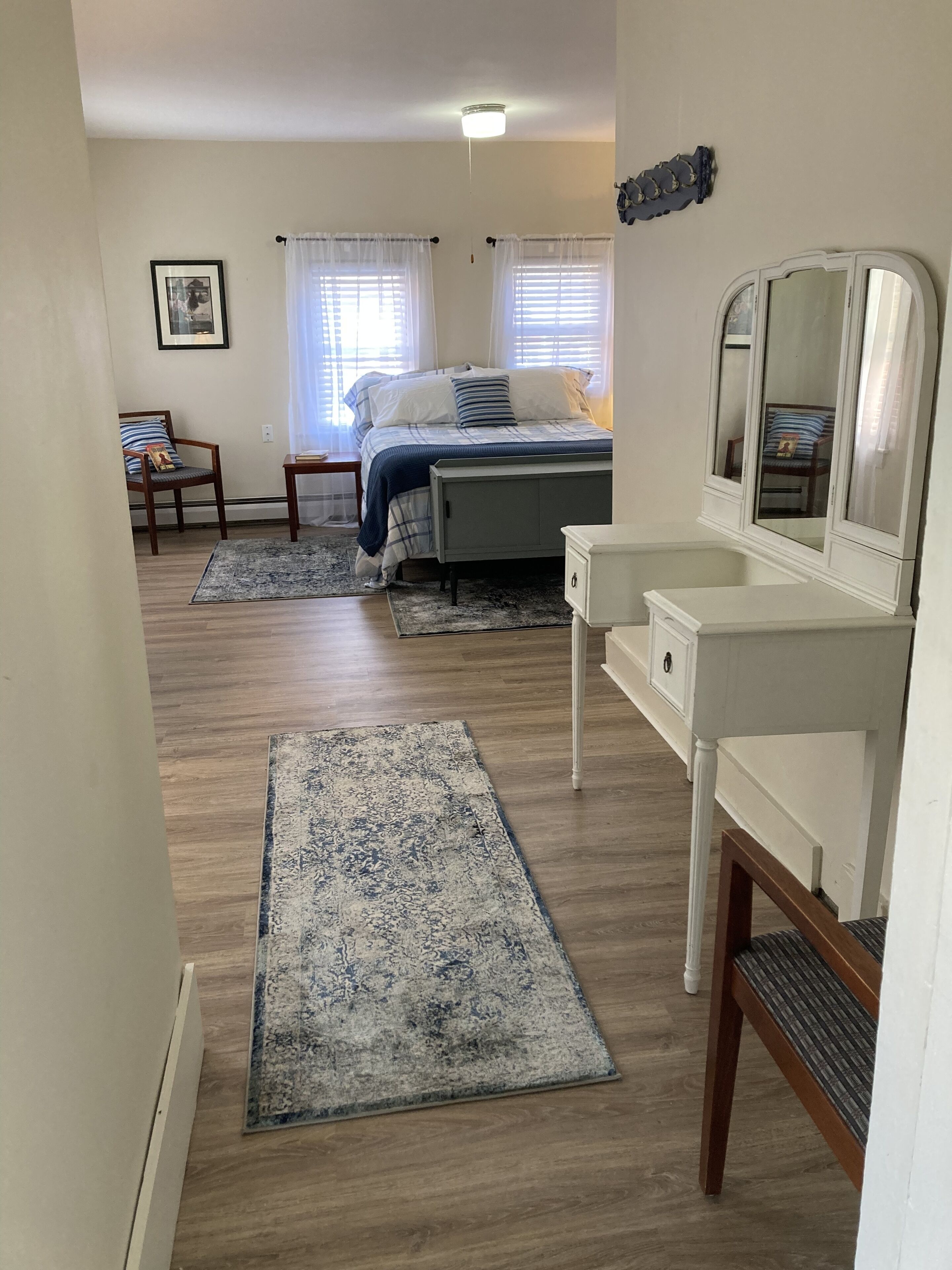 Un dormitorio con cama, mesita de noche, silla y un espejo grande.