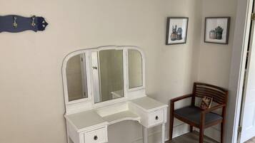 Een witte kaptafel met spiegel, een houten stoel en twee afbeeldingen in lijsten aan de muur.