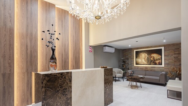 A modern reception area with a marble counter, a chandelier, a painting on the wall, and a seating area with a sofa and chairs. - Equo Hotel Boutique (Lima)