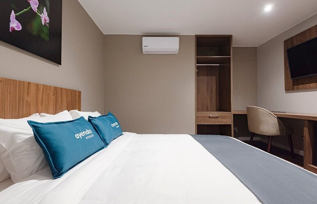 Habitación de hotel con cama, escritorio, silla, armario y aire acondicionado.