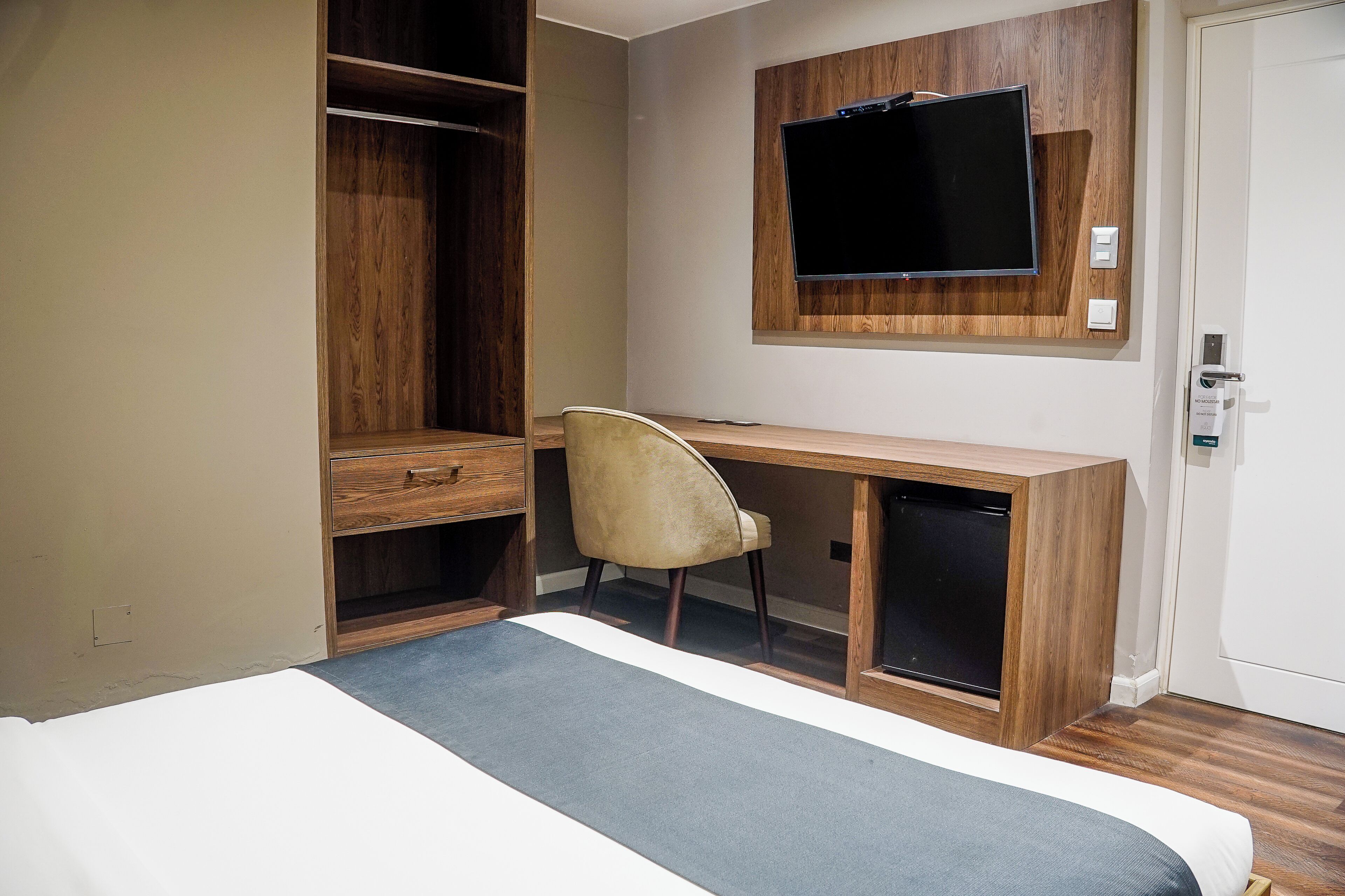 Una habitación de hotel con cama, escritorio, silla, televisor y armario.