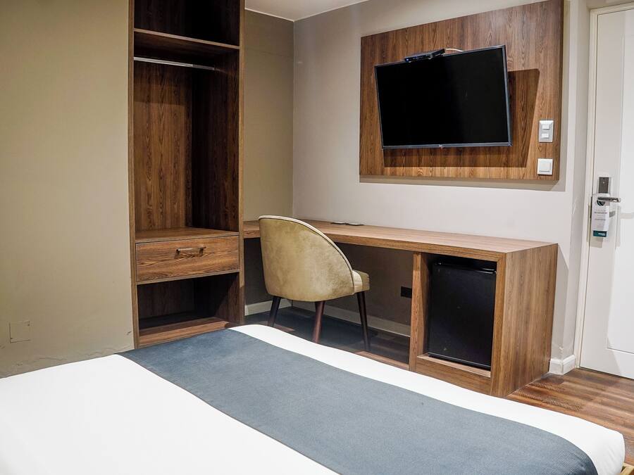 Una habitación de hotel con cama, escritorio, silla, televisor y armario.