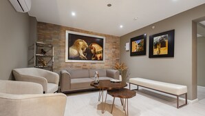 A modern living room with a sofa, two armchairs, a coffee table, and a bench. There are three framed pictures on the wall and a small shelf with decorative items. - Equo Hotel Boutique (Lima)