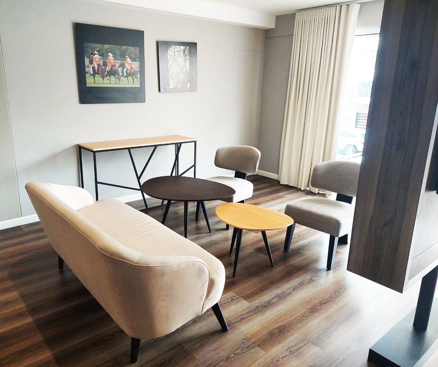 Una sala de estar moderna con un sofá, dos sillones, una mesa baja y una pequeña mesa con sillas. Hay dos cuadros enmarcados en la pared.