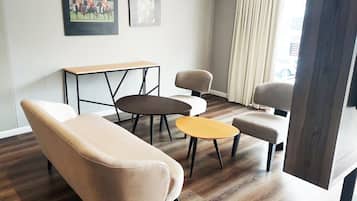 Una sala de estar moderna con un sofá, dos sillones, una mesa baja y una pequeña mesa con sillas. Hay dos cuadros enmarcados en la pared.