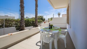 A balcony with a table set for two, surrounded by white chairs, palm trees, and a clear sky. - VILLA ISCHIA - Villa a few meters from the sea (Torre Suda)