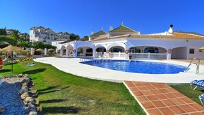 A pool area with a clear blue pool, a white building with arches, and a tiled walkway. - SHR004 Smile Beach House. Incredible views. (Nerja)