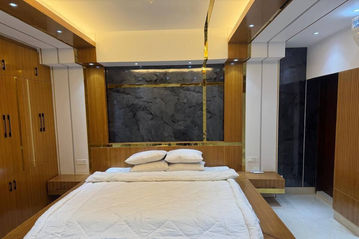 A modern bedroom with a large bed, wooden wardrobe, and a marble accent wall.
