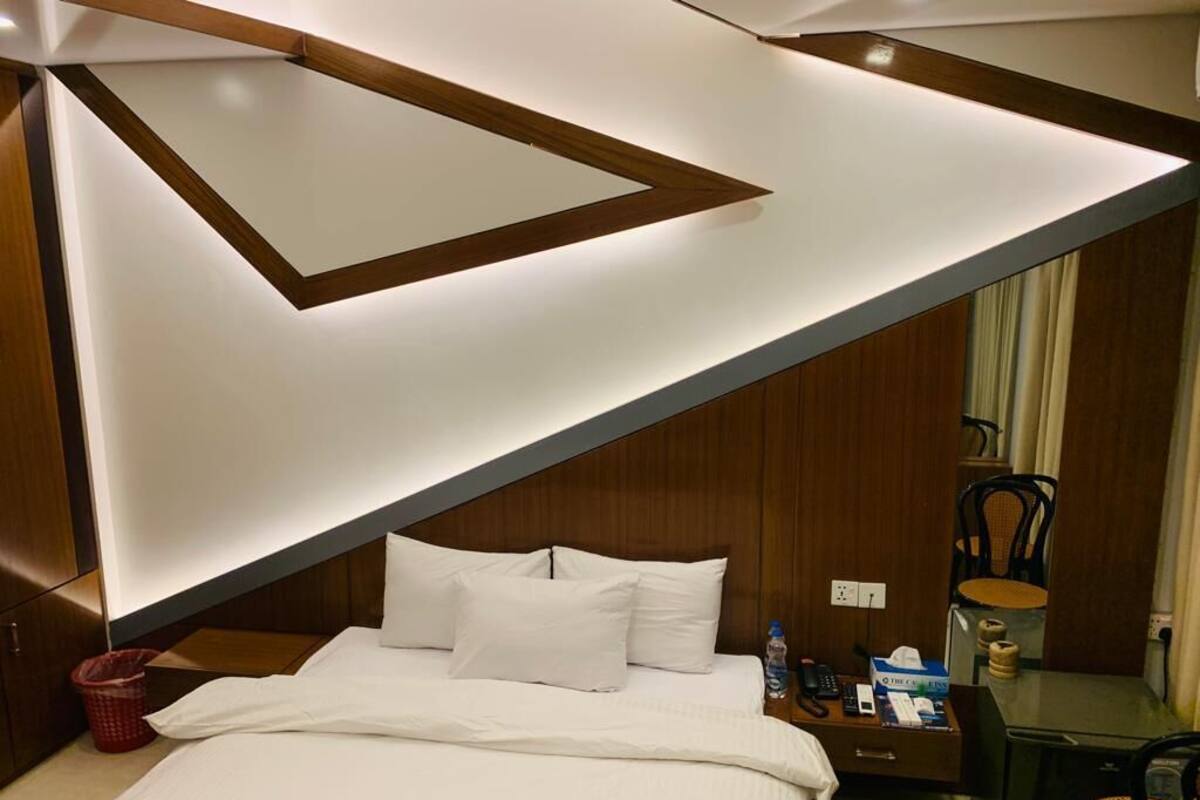 A modern hotel room with a bed, bedside table, and a desk with a chair.