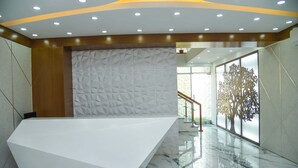A modern lobby with a geometric-patterned wall, a white reception desk, and a glass staircase. -  The Castle Inn Hotel & Restaurant Uttara Dhaka (Dhaka)