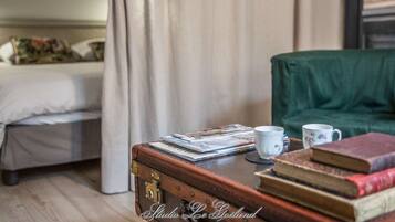 A room with a bed, a green chair, a wooden table with books and a mug, and a suitcase.