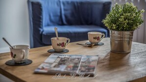 Une table en bois, un magazine, deux tasses à thé ornées de motifs floraux, une cuillère et une plante en pot.