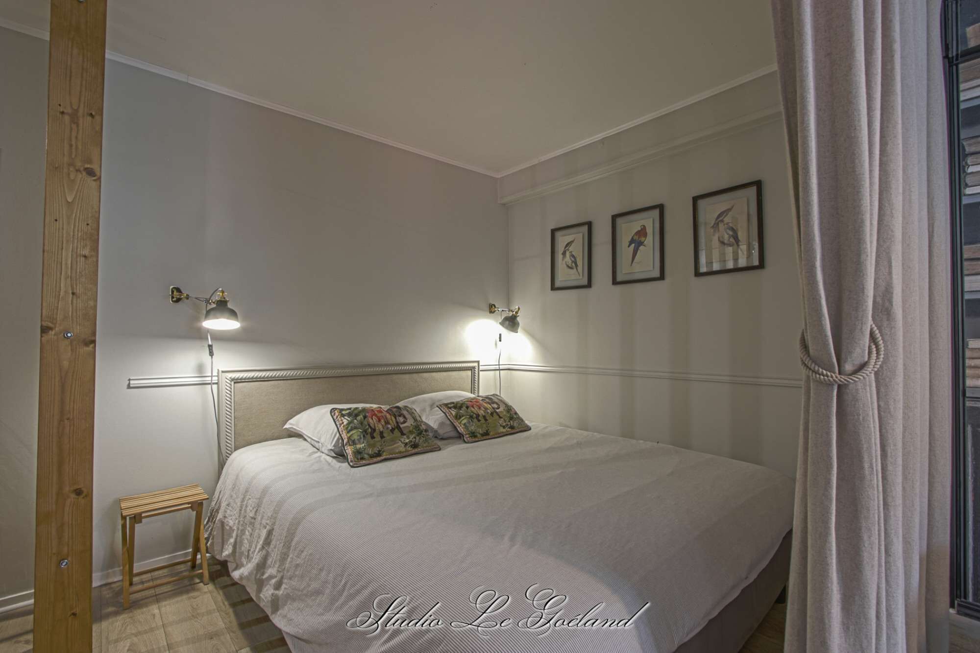A neatly arranged bedroom with a bed, two bedside lamps, a small table, and framed pictures on the wall.
