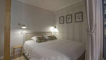 A neatly arranged bedroom with a bed, two bedside lamps, a small table, and framed pictures on the wall.