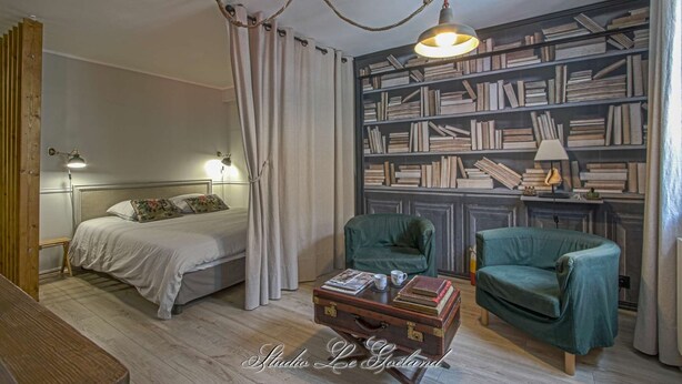 Une chambre à coucher avec un lit, une lampe de chevet, un fauteuil vert, une commode en bois et une bibliothèque remplie de livres.
