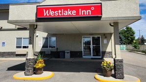 The exterior of the Westlake Inn, featuring a prominent red sign, a covered entrance, and two potted plants. - Westlake Inn (Strathmore)