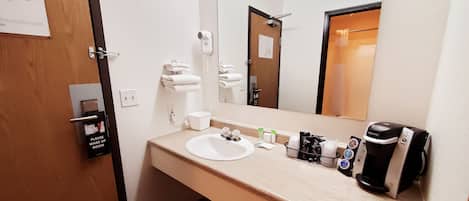 Un baño de hotel con lavamanos, perchero para toallas, secador de pelo, espejo y cafetera.