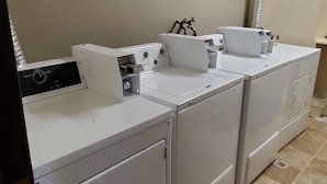 A laundry room with four stacked front-loading washing machines and a dryer. - Westlake Inn (Strathmore)
