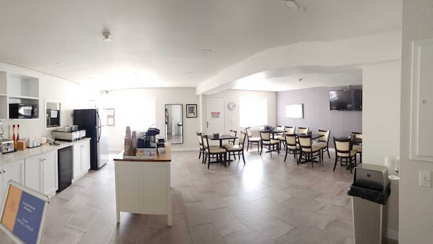 A modern kitchen with a built-in microwave, a coffee machine, and a refrigerator. There is a dining area with a table and chairs. - Westlake Inn (Strathmore)