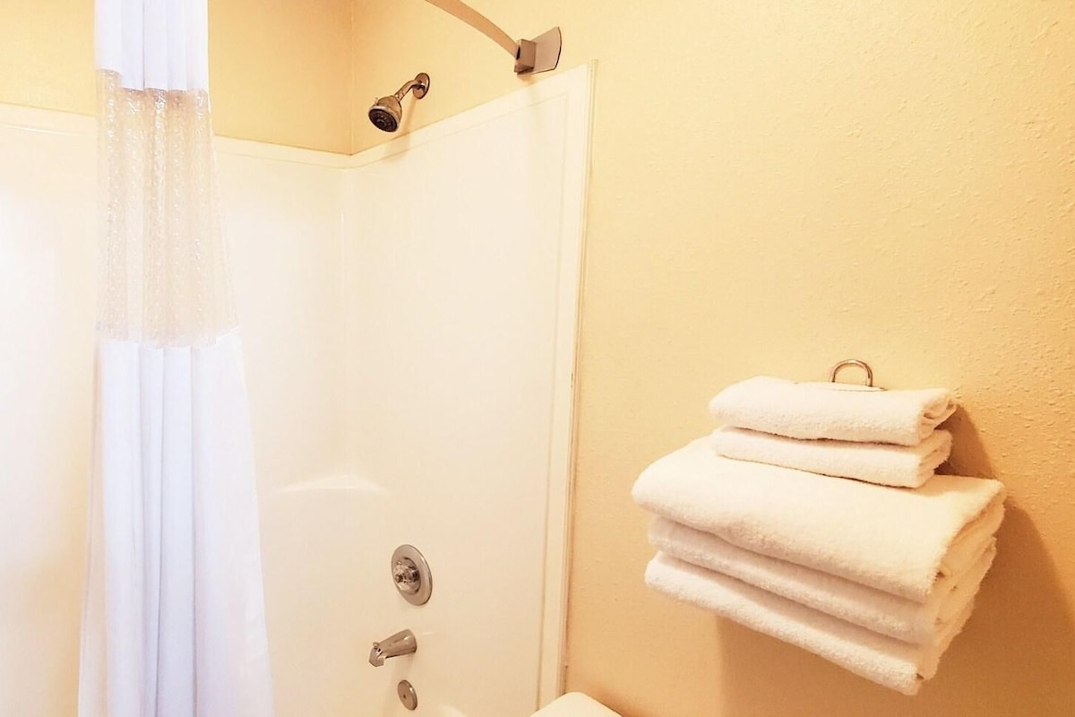 A shower with a curtain, a towel rack with folded towels, and a wall-mounted showerhead.