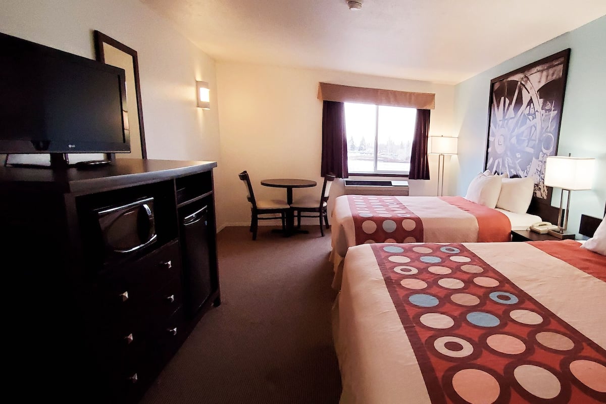 Habitación de hotel con dos camas, televisión, escritorio y ventana con cortinas.