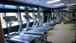 Une salle de sport avec plusieurs tapis de course alignés en rangées, un panneau de commande et du matériel d’exercice.
