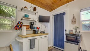 A kitchen with a wooden ceiling, a TV mounted above the counter, a microwave, and a window with a view of greenery. - Private Tiny House Retreat with Spacious Patio, Free Parking & WiFi (Las Vegas)